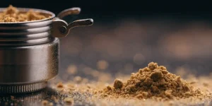 Golden Cannabis Kief Powder Next to a Metal Grinder