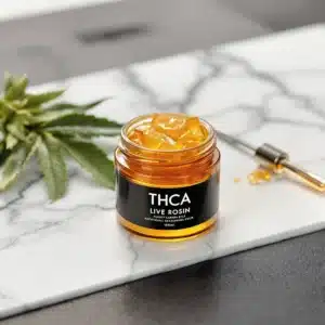 Golden THCA live rosin in a jar with cannabis leaves and a dab tool.
