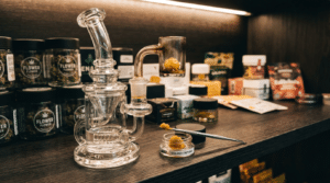 Dab rig with cannabis concentrates shelf display featuring a glass rig, quartz banger, wax jar, and retail cannabis products.