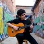 Top pre roll reviews street guitar smoker playing acoustic guitar in graffiti alley with lit pre-roll.