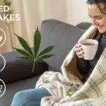 Woman sitting on a couch wrapped in a blanket, holding a cup of tea and smiling, with cannabis icons and text indicating mild weed shakes