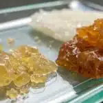 Realistic close-up of live resin and rosin samples on a glass surface, emphasizing distinct textures and colors.