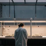 Scientist in a lab coat observing a 3D model of a cannabis plant in a laboratory setting.