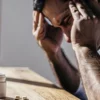 Man holding his head in pain, with a bottle of pills on a table