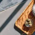 Overhead shot: rustic wooden tray with a small bowl of cannabis and a larger bowl of salt.