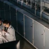 Two researchers in lab coats examining cannabis biotech equipment under lab lighting.