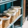 High-angle shot: blue wooden shelf filled with straw baskets containing various dried goods, by an entrance.