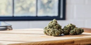 Close-up of two cannabis buds on a wooden cutting board, kitchen background.