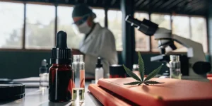 A cannabis leaf and oil bottles on a lab table, a scientist working in the background.