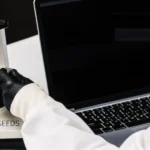 Scientist analyzing a cannabis sample under a microscope labeled Blimburn Seeds next to a laptop.