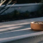 Wooden bowl filled with cannabis seeds on a stone ledge outdoors.