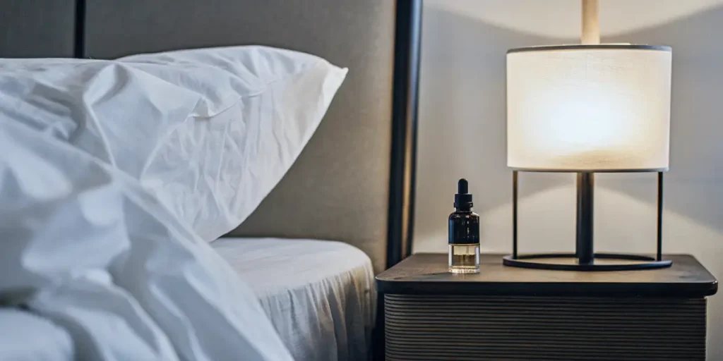 CBD oil bottle on a nightstand beside a neatly made bed.
