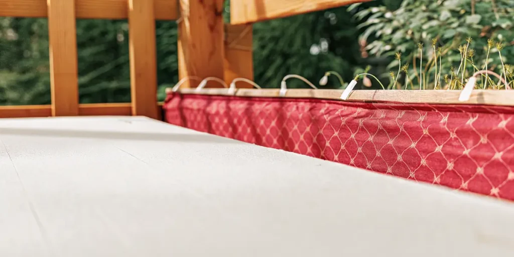 Red flower bed with green sprouts placed on a wooden balcony railing.
