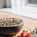 Wooden bowl filled with terpene-heavy strawberry cannabis seeds next to fresh strawberries.