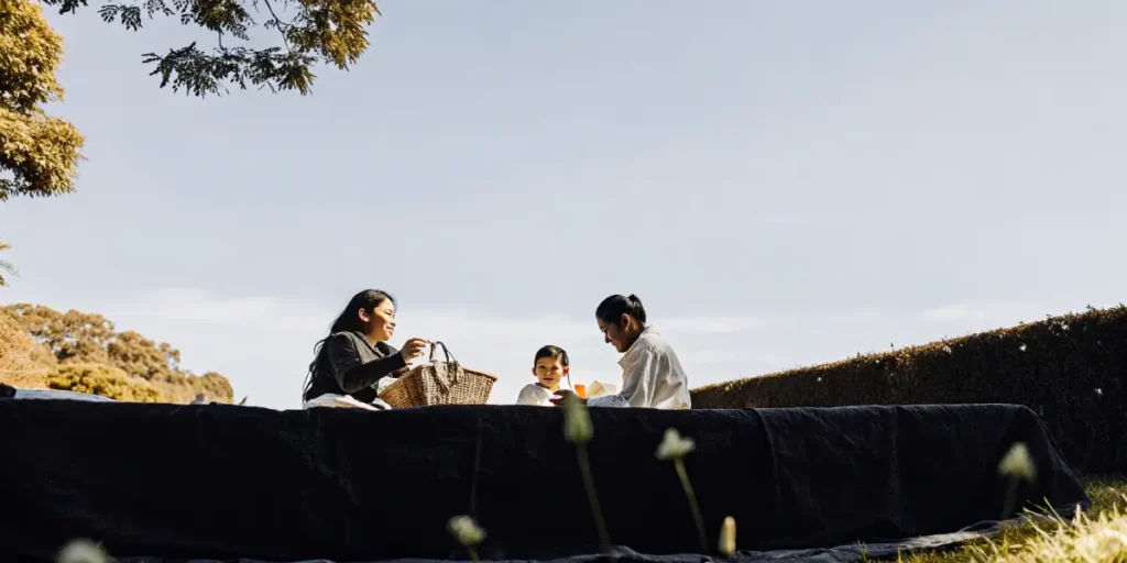 Family enjoying a peaceful outdoor picnic on a sunny day with trees and open sky surrounding them.