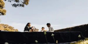 Family enjoying a peaceful outdoor picnic on a sunny day with trees and open sky surrounding them.