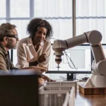 A diverse team of engineers collaborating around an advanced robotic arm in a modern lab.