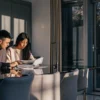 A couple sitting at a modern dining table reviewing documents together in soft evening light.