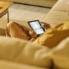 Man sitting comfortably on a sofa while browsing a tablet in a softly lit living room.