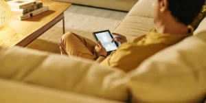 Man sitting comfortably on a sofa while browsing a tablet in a softly lit living room.