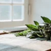 Mint cannabis flowers and leaves resting on a wooden table near a window, with soft natural light highlighting texture.