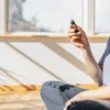 Person sitting on the floor holding a CBD oil bottle during a relaxing aromatherapy session by a sunlit window.