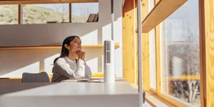 Woman sitting at a desk in a bright office, looking out the window with a thoughtful expression.