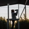 Field worker using a refractometer to analyze cannabis plants in a large outdoor cultivation under shade netting.
