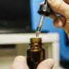 Hand using a dropper to dispense cannabinoid oil into a glass bottle in a laboratory setting.