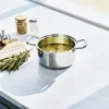Stainless steel pot with cannabis-infused butter melting on a modern kitchen countertop alongside fresh herbs and cooking utensils.