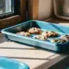 Cannabis-infused chocolate chip cookies cooling in a blue baking tray on a sunlit kitchen countertop.