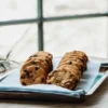 Cannabis-infused chocolate chip cookies neatly arranged on a metal tray near a sunlit window with a cannabis leaf beside them.