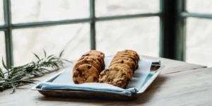 Cannabis-infused chocolate chip cookies neatly arranged on a metal tray near a sunlit window with a cannabis leaf beside them.