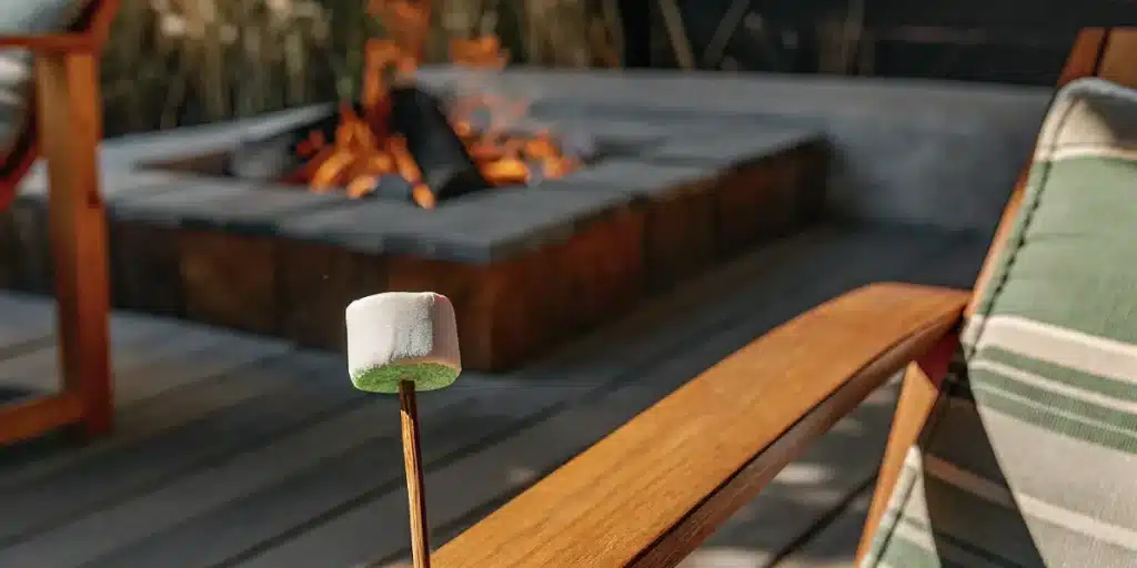 Cannabis-infused marshmallow on a wooden stick roasting near an outdoor fire pit at sunset