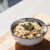 Steaming bowl of cannabis-infused rice topped with ground flower on a wooden cutting board near a sunlit window.
