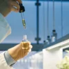 Scientist using a dropper to extract cannabis oil into a glass vial inside a controlled laboratory environment