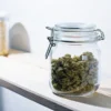 Glass jar filled with dried cannabis buds placed on a wooden shelf in a clean storage space.