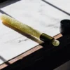 Green THC-infused lollipop resting on a marble surface with natural light and a dropper cap nearby.