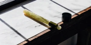 Green THC-infused lollipop resting on a marble surface with natural light and a dropper cap nearby.