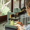 Scientist examining a cannabis sample under a laboratory microscope near a window.