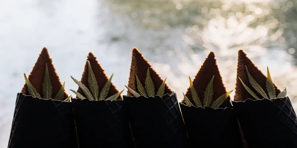 Weed-infused dessert cones decorated with cannabis leaves and triangular biscuits arranged in a row.
