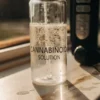 Glass vial labeled cannabinoid solution with bubbles under natural light in laboratory setting.