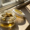 Cannabis concentrate jar sunlight window with thick extract inside a glass container on a windowsill.