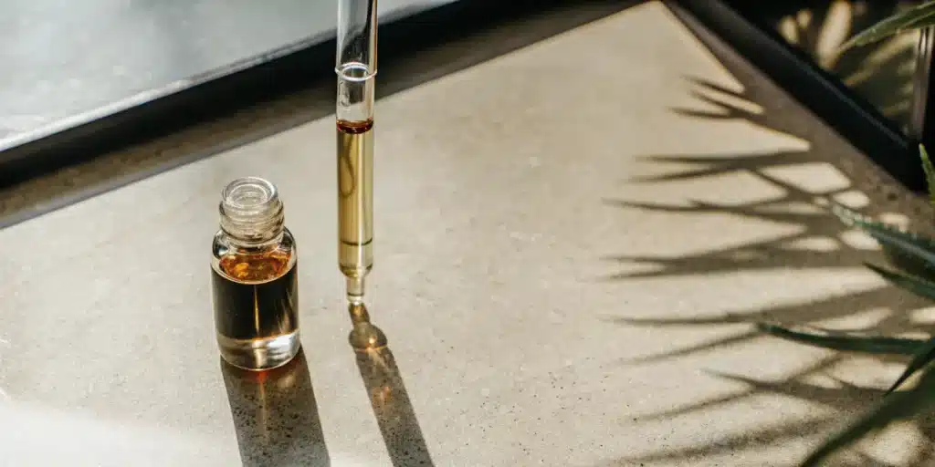 Cannabis extract dropper with amber oil dripping into glass vial on laboratory surface.