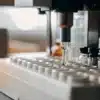 Automated machine filling small vials with cannabis extract in laboratory setting.
