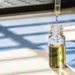 Cannabis oil dropper above glass vial with golden extract in natural sunlight.