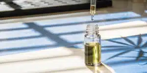 Cannabis oil dropper above glass vial with golden extract in natural sunlight.
