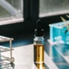 Cannabis oil vial next to laboratory test tubes with blue liquid on bench.