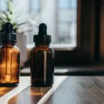 Amber glass dropper bottles for cannabis tincture on wooden surface with sunlight.