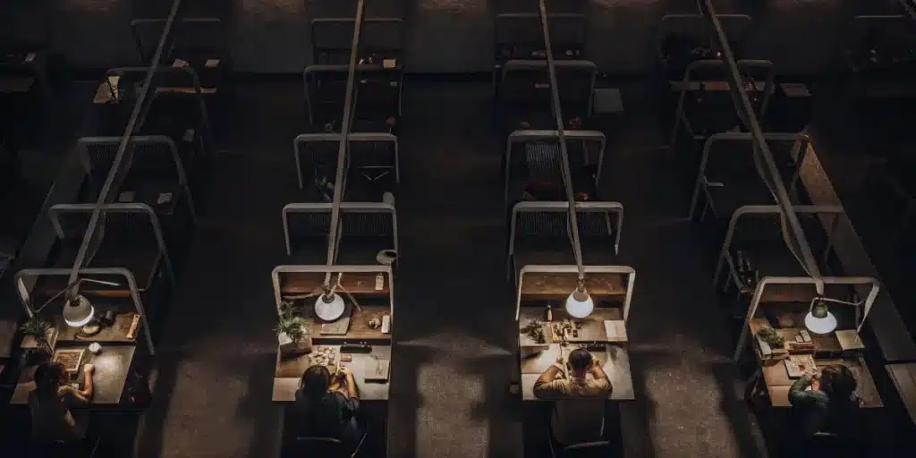 Workers trimming cannabis at individual workstations in an indoor facility.